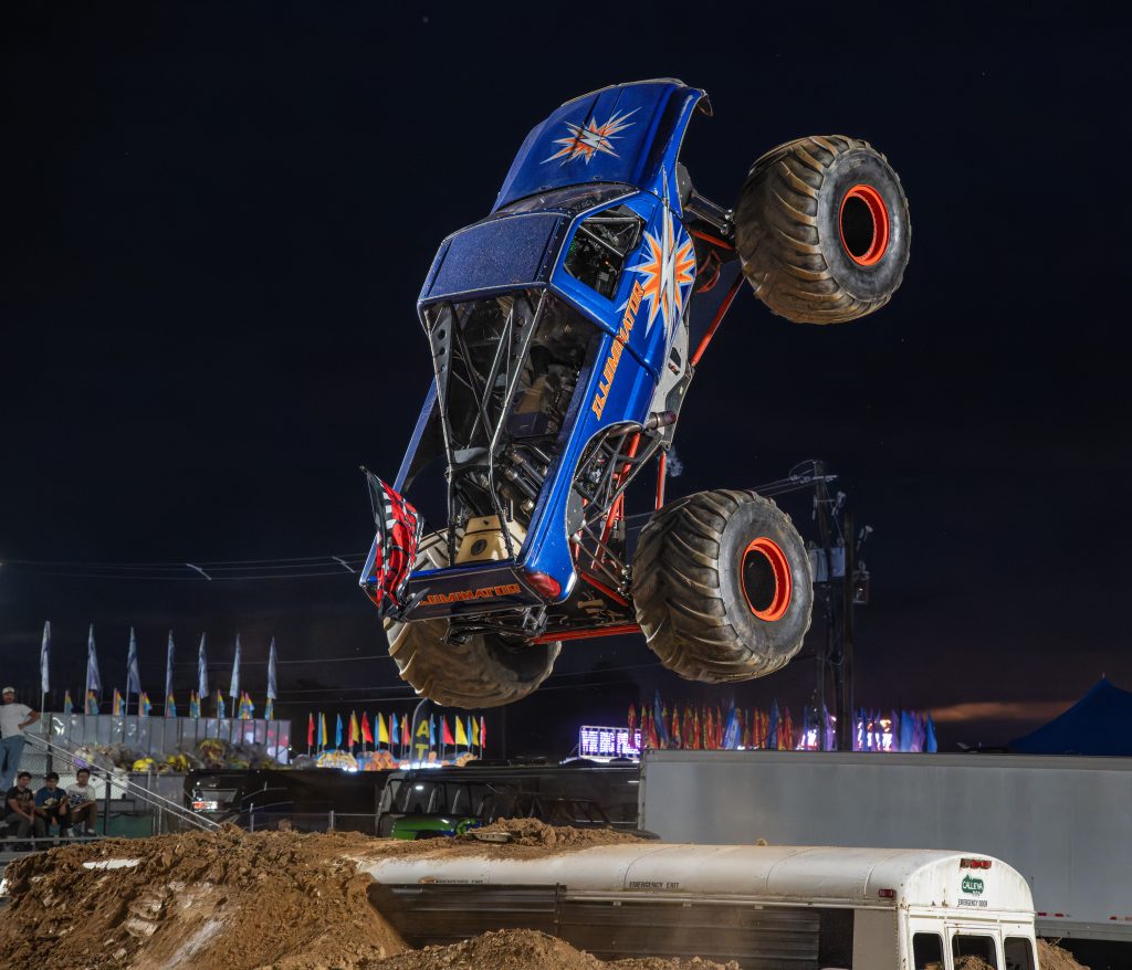 Illuminator Monster Truck performing a huge sky wheelie over a junk school bus during the freestyle competition 